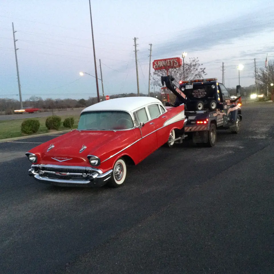 Red and white 1957 Chevy Bel Air on the hook behind Joey's wrecker at dusk