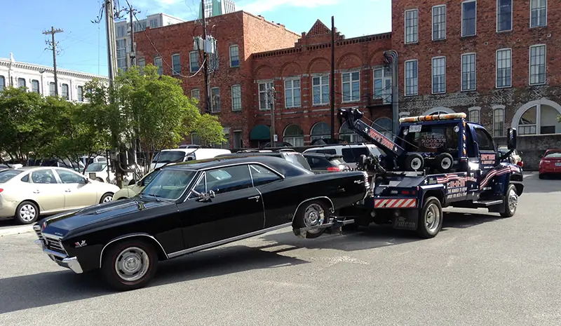 Joey's wrecker towing a black Chevelle past old brick buildings