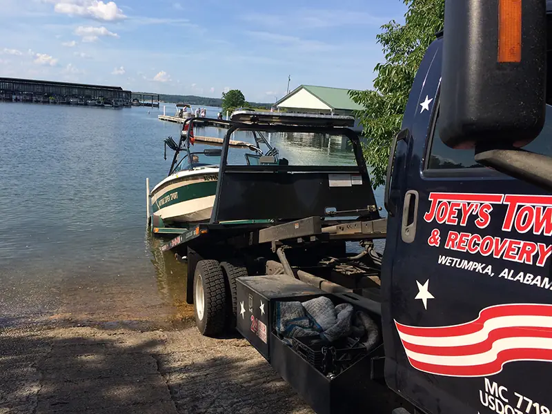 Joey's flatbed backed down a lake boat ramp with a boat on the bed