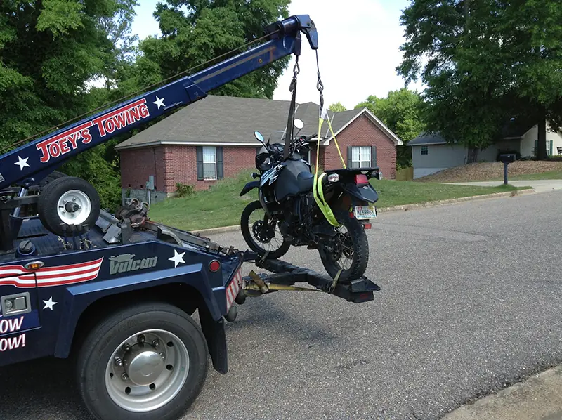 Side view of a motorcycle being towed on Joey's wrecker with the boom raised