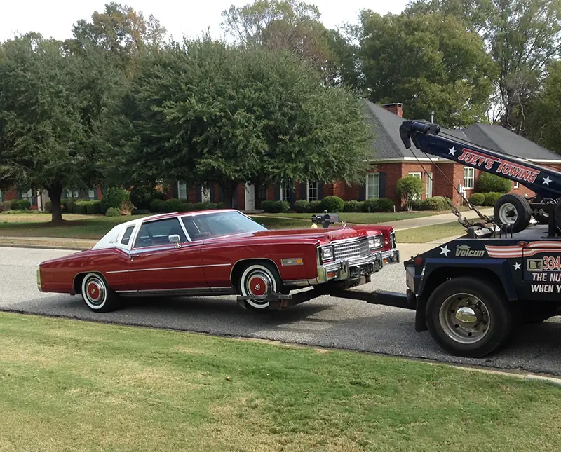 Red Cadillac Eldorado being towed by Joey's wrecker on a grassy street