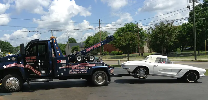 Joey's wrecker towing a white first-generation Corvette down a residential street