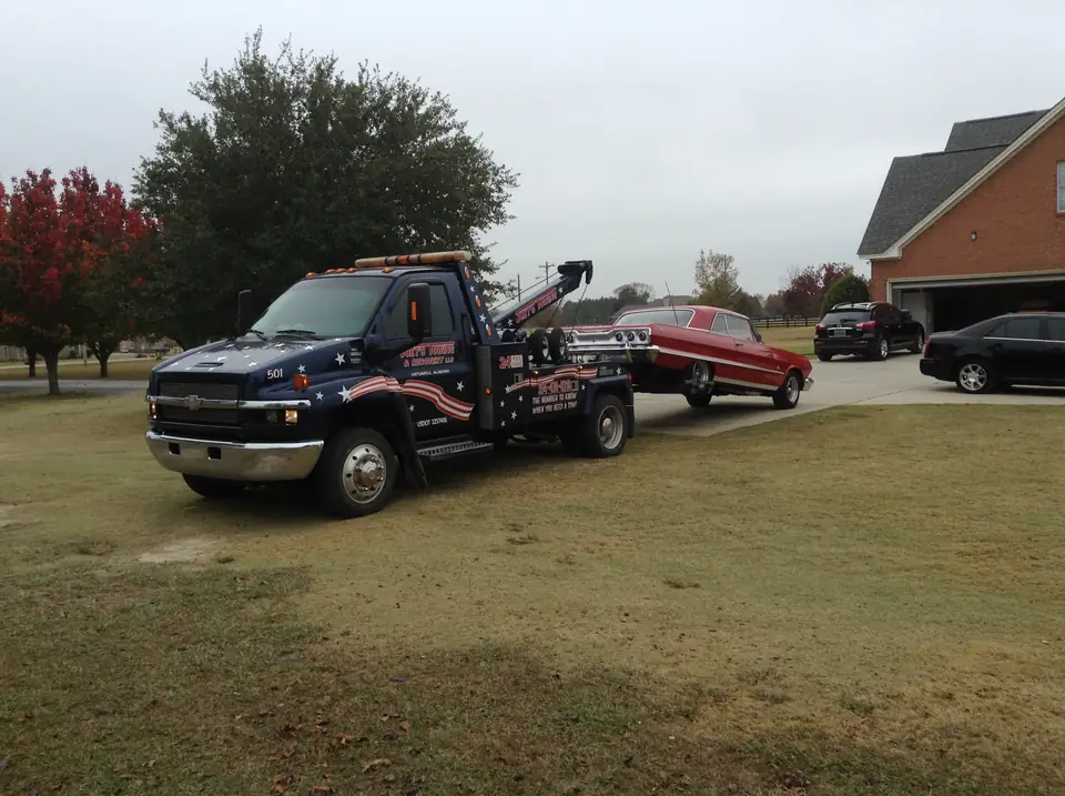 Joey's navy wrecker with flag striping towing a red classic Chevy across a lawn